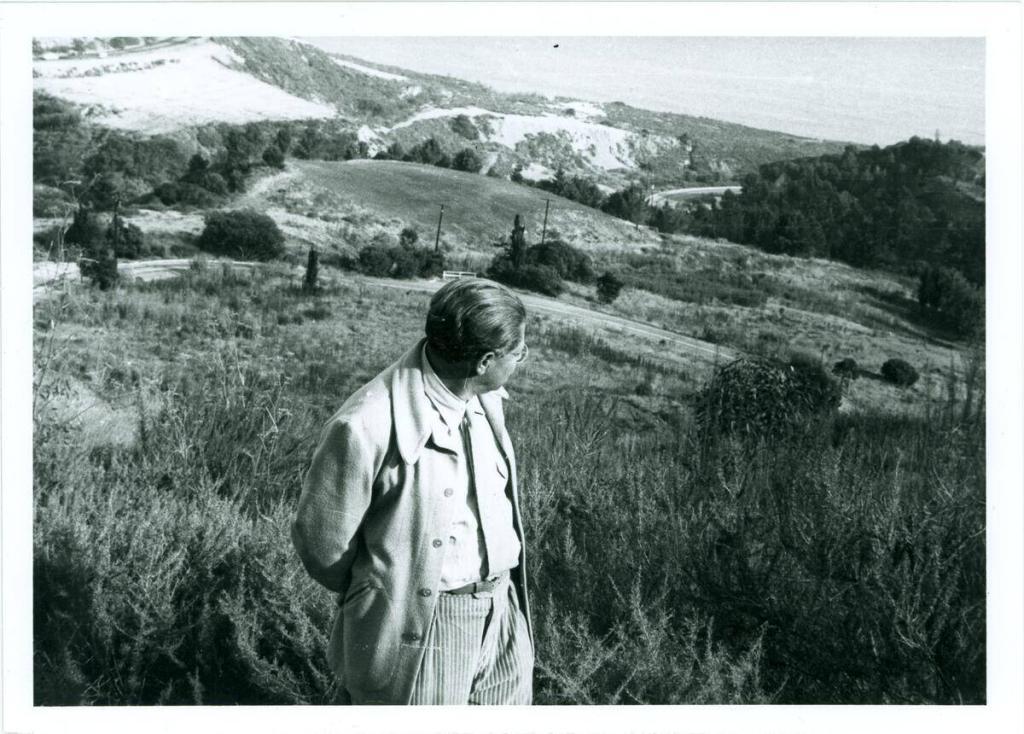 Foto von Lion Feuchtwanger, aufgenommen von der Seite, während er über seine Schulter schaut, mit dem Meer und den Hügeln im Hintergrund, in Pacific Palisades.