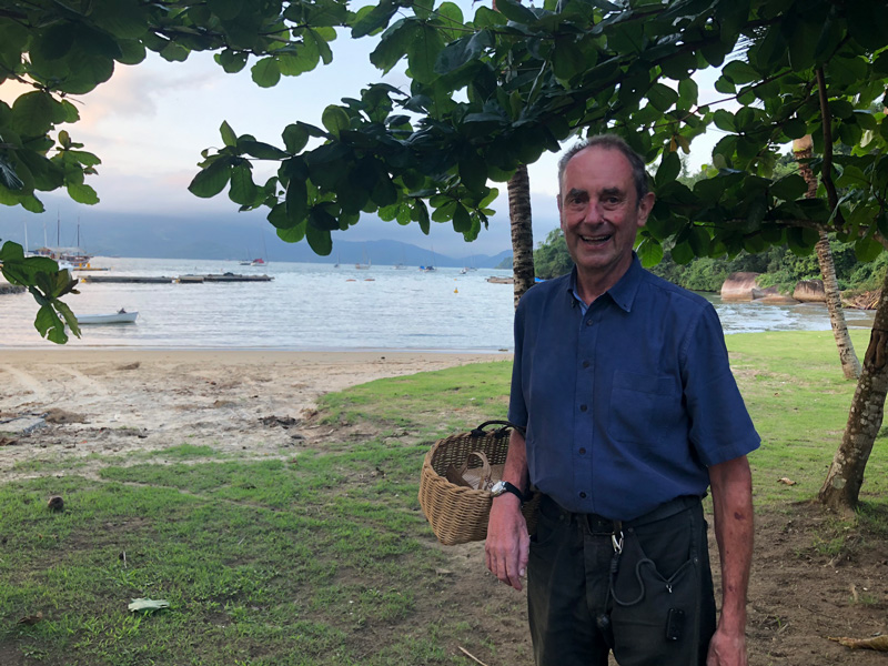 Lachender, älterer Mann am Strand mit Korb im rechten Arm