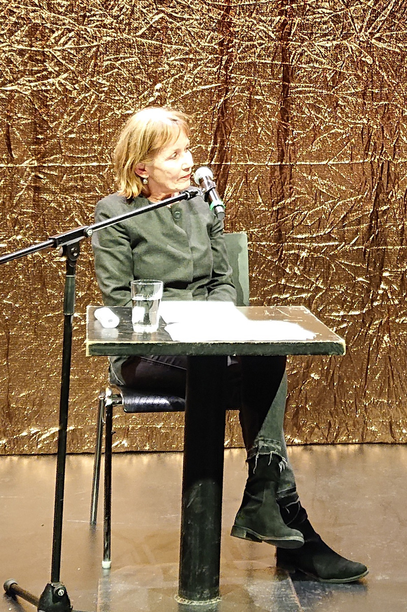 Vor einem goldenen Grund auf einem Podium sitzt eine ältere Damen und blickt nach rechts: Dagmar Leupold.