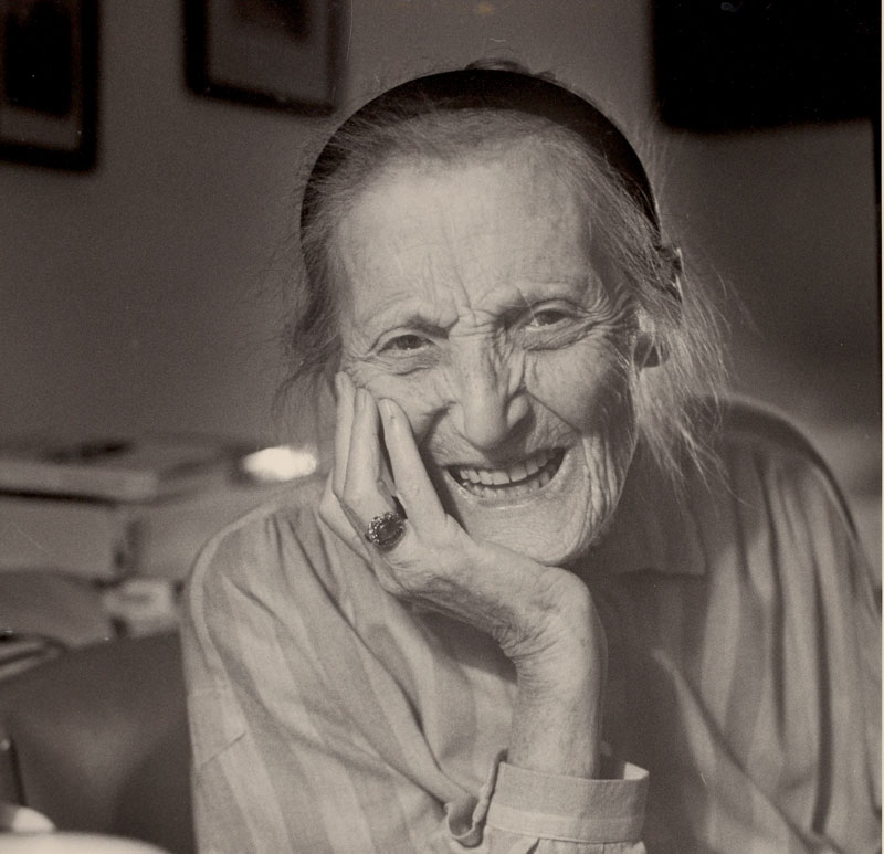 Porträt einer alten Dame mit Haarreif, Kinn aufgestützter Hand mit Ring, blickt lächelnd in die Kamera: Gerty Spies.