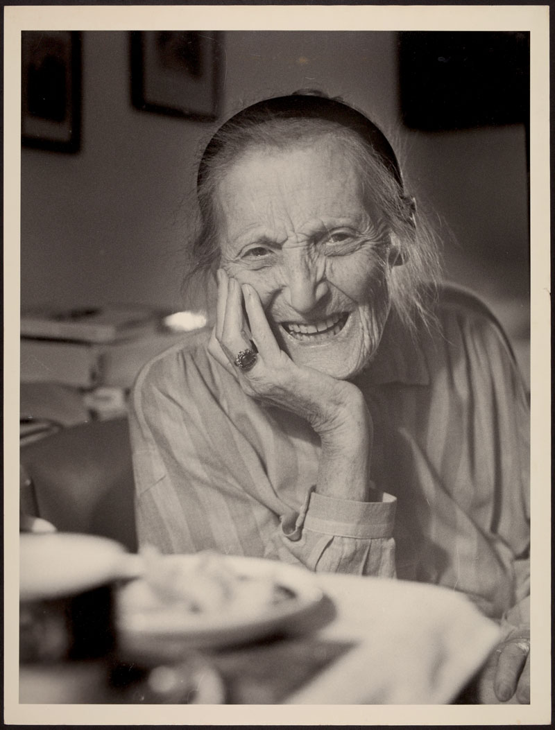 Porträt einer alten Dame mit Haarreif, Kinn aufgestützter Hand mit Ring, blickt lächelnd in die Kamera: Gerty Spies.