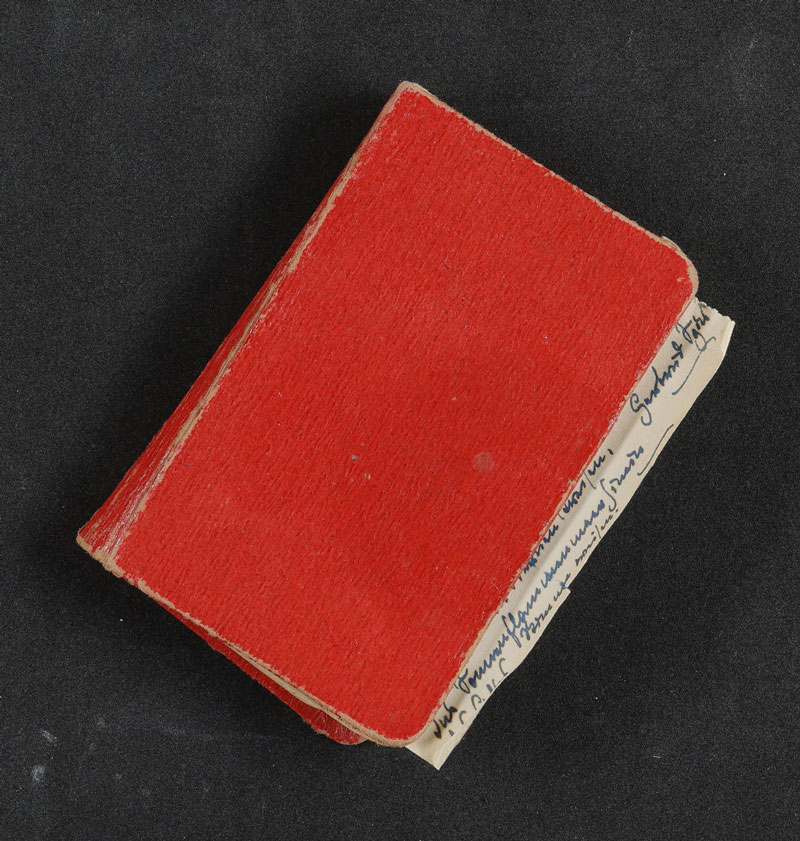 Rotes Notizbuch mit beschriebenen Blatt herausschauend auf schwarzem Grund. Gerty Spies' Notizbuch