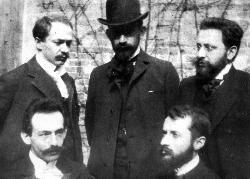 Historisches Foto: Drei Männer stehend, davor zwei sitzend: Gründer des Jüdischen Verlags 1902, sitzend Berthold Feiwel, Martin Buber; stehend E. M. Lilien, Chaim Weizmann, Davis Trietsch (gemeinfrei)