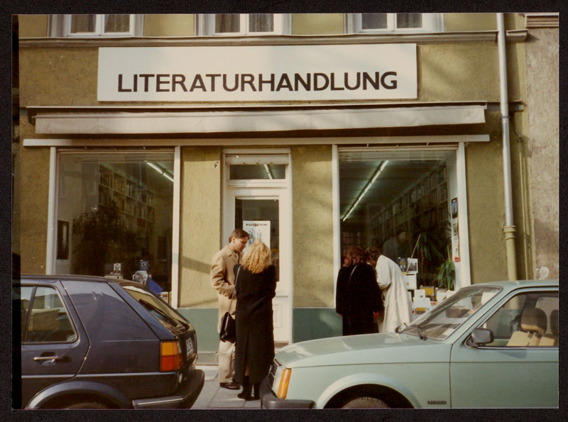 Blick auf die Buchhandlung Literaturhandlung in München mit einem Päarchen vor der Tür und zwei Frauen, die sich die Fensterauslagen anschauen, davor zwei Autos