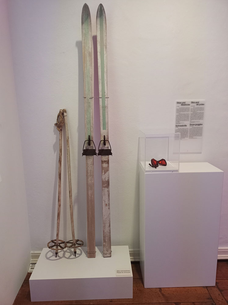 An Wand gelehnte Skier, Skistöcke und Skibrille in Vitrine. Blick in die Thomas Mann-Ausstellung in Lübeck