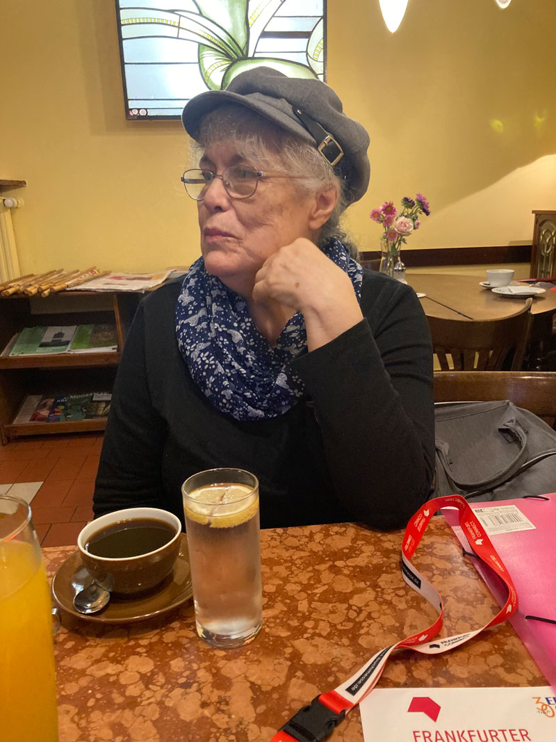 Dorita Puig sitzt am Tisch mit Café und Wasserglas vor sich, ALAM-Autorin