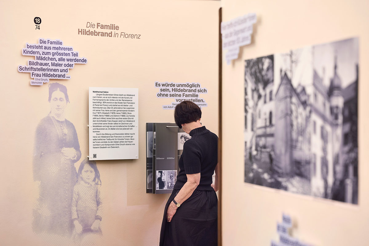 Frau steht an einer Bilderhalterung in einer Ausstellung, beschriftet mit "Die Familie Hildebrand in Florenz".