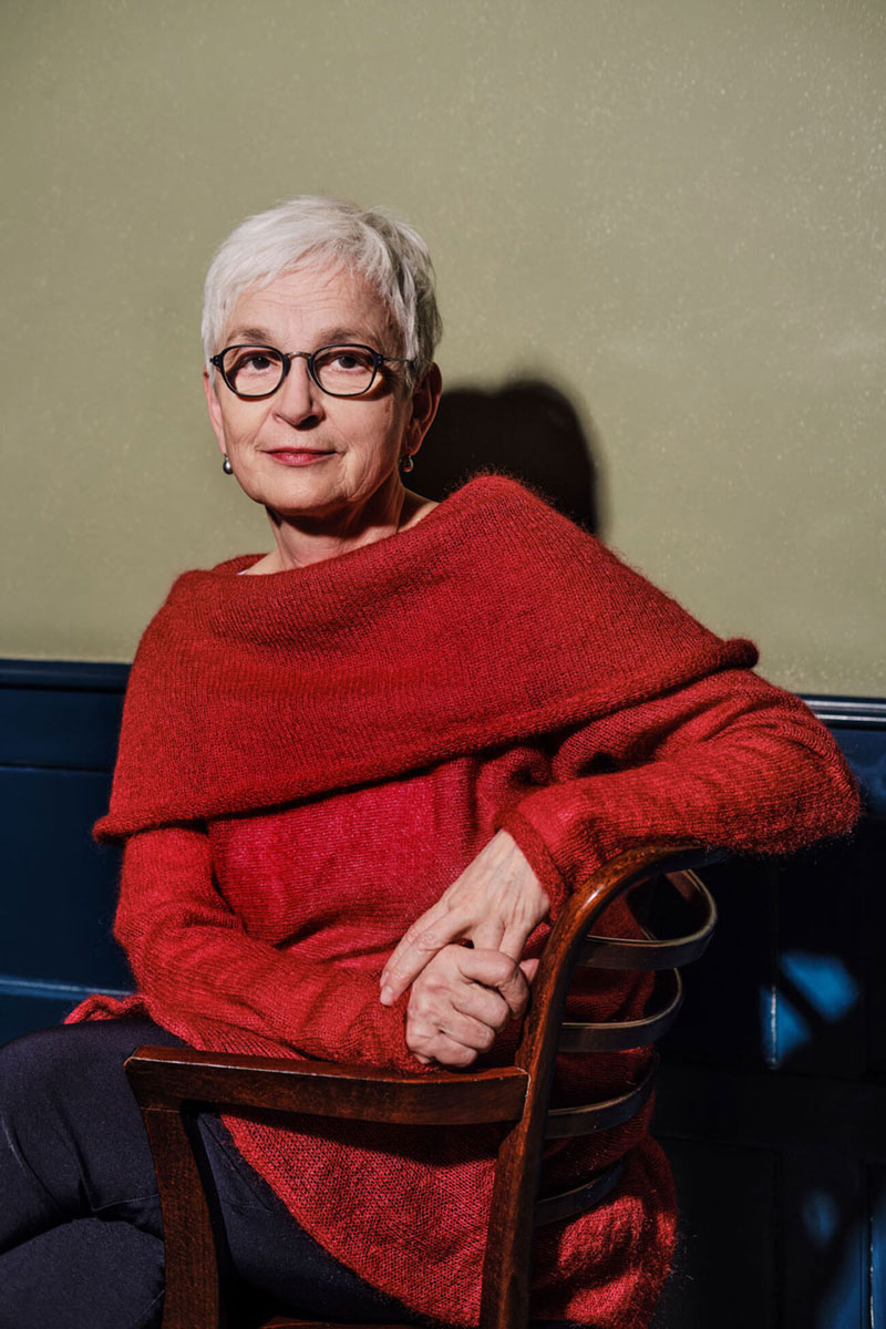 Porträt einer älteren sitzenden Frau mit roten Pullover und Brille: Barbara Mundel