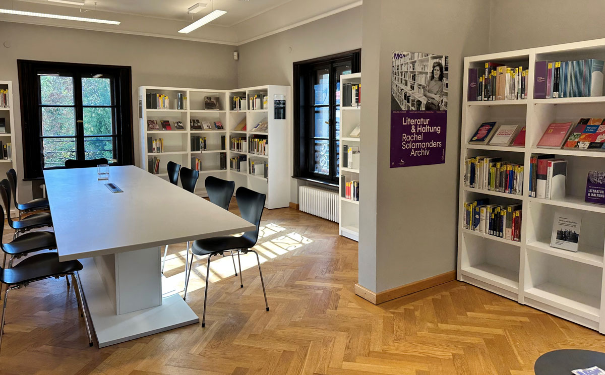 Blick in die Familie Mann-Bibliothek. Sonnenlicht fällt ein, Stühle und Lesetisch mit ganz vielen Büchern in den Regalen. Monacensia-Bibliothek