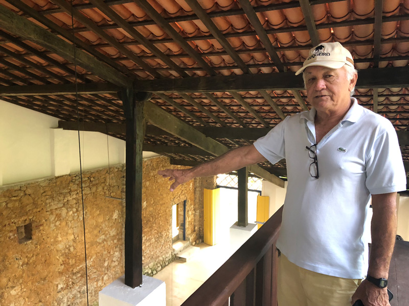 Älterer, weißhaariger Mann mit Kappe, der im Inneren eines Hauses auf etwas hinweist: Eduardo José Mello.