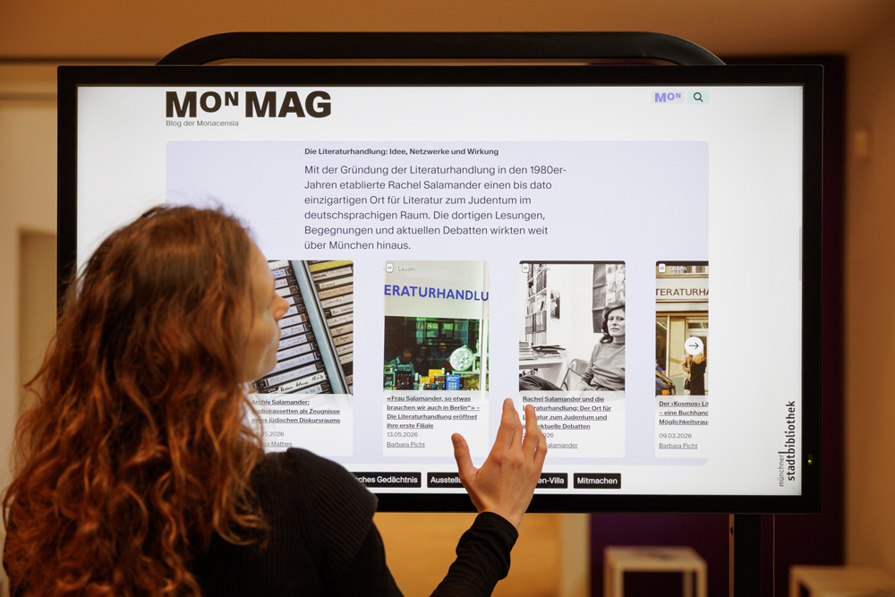 Frau vor einem Touch-Screen mit MON Mag und Artikeln, scrollt. Literaturhandlung Rachel Salamanders.