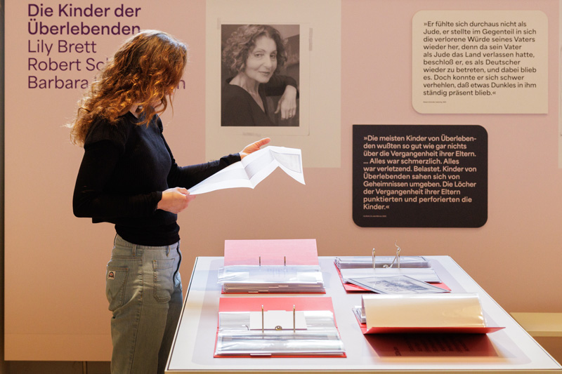 Frau in Ausstellung Literatur & Haltung. Rachel Salamanders Archiv. Blättert in ausliegenden roten Ordnern.
