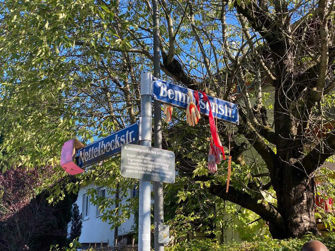 Aktion gegen koloniale Straßennamen in München: Mit Kunstblut befüllte Handschuhe hängen am Straßenschild "Benningsenstraße".