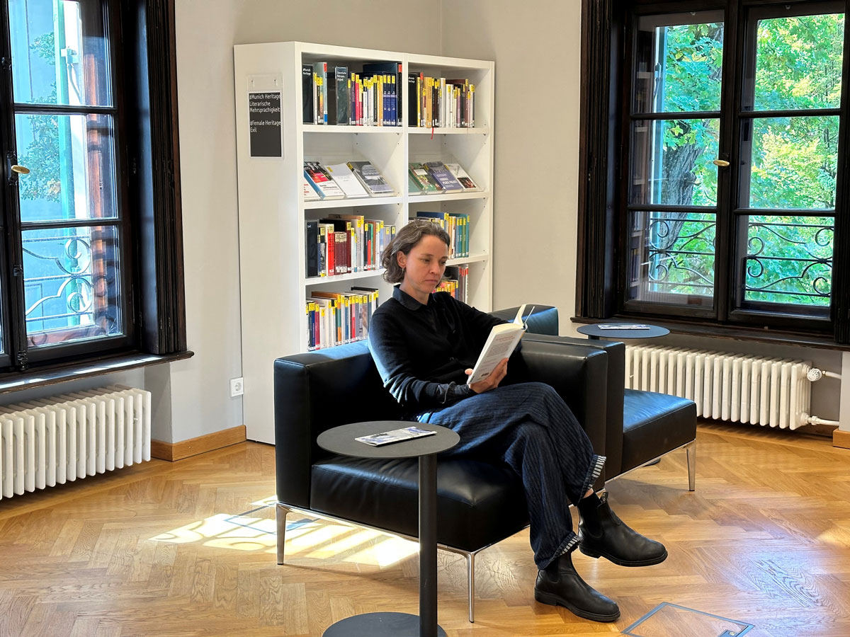 Larissa Schmid sitzt auf einem Sessel lesend in der Familie Mann Bibliothek der Monacensia