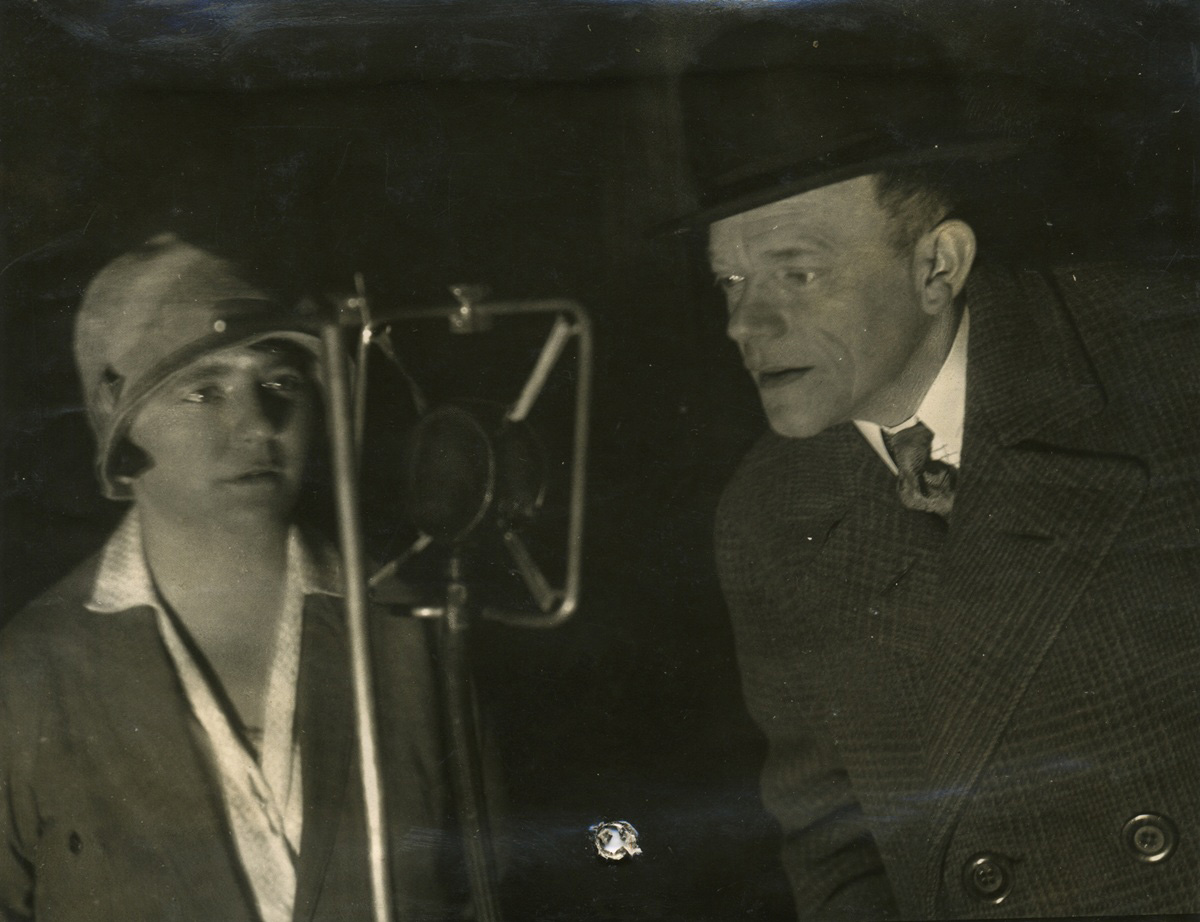Zwei Menschen: links: Frau, rechts: Mann mit Melonenhut, sprechen in ein Mikrofon, um 1929: Karl Valentin und Liesl Karlstadt.