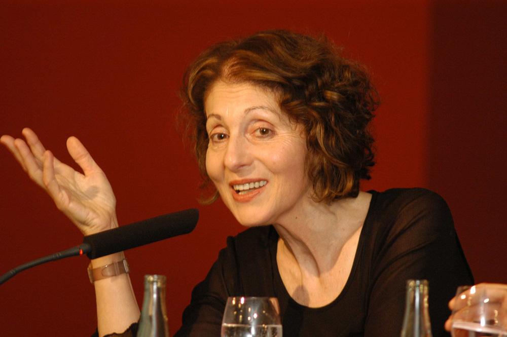 Eine mittelalte Frau sitzt vor einem Mikrofon, rechte Hand gestikuliert, freundlich in einer Rede: Lily Brett.