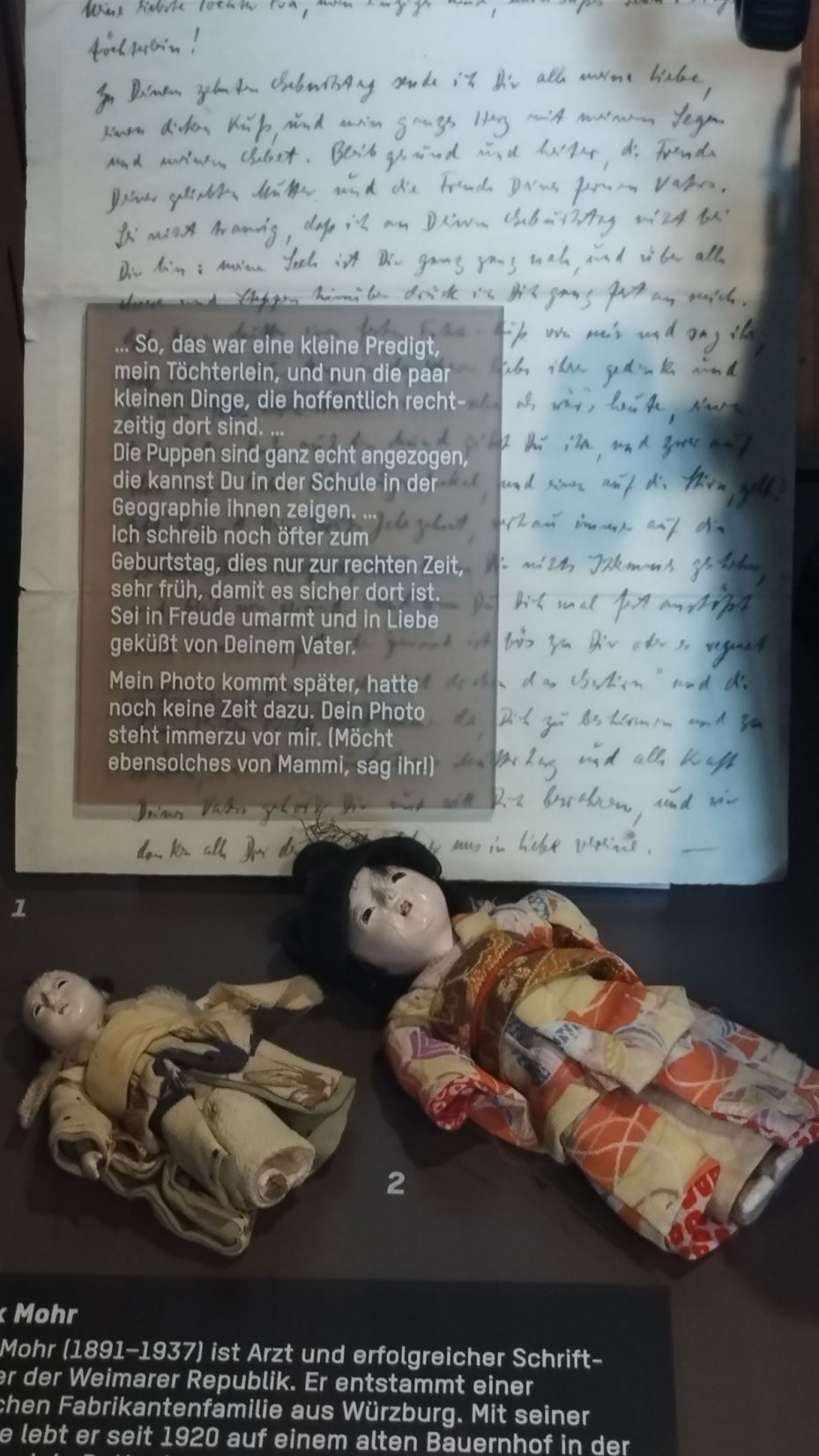Blick in Ausstellungsvitrine: Puppen aus Shanghai, Geschenk von Max Mohr an seine Tochter, dahinter ein Brief von ihm an die Tochter.