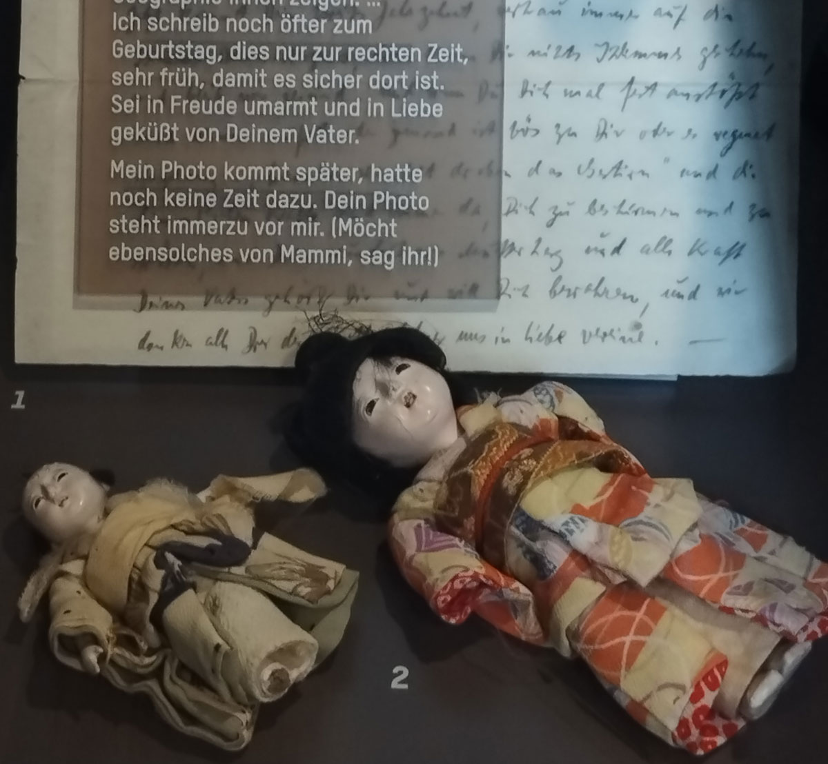 Blick in Ausstellungsvitrine: Puppen aus Shanghai, Geschenk von Max Mohr an seine Tochter, dahinter ein Brief von ihm an die Tochter.