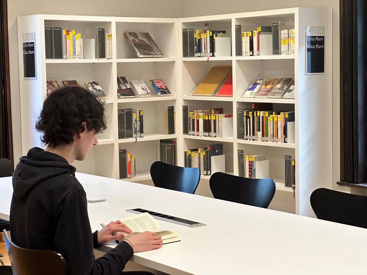 Junger Mann liest in einer Bibliothek ein Buch.