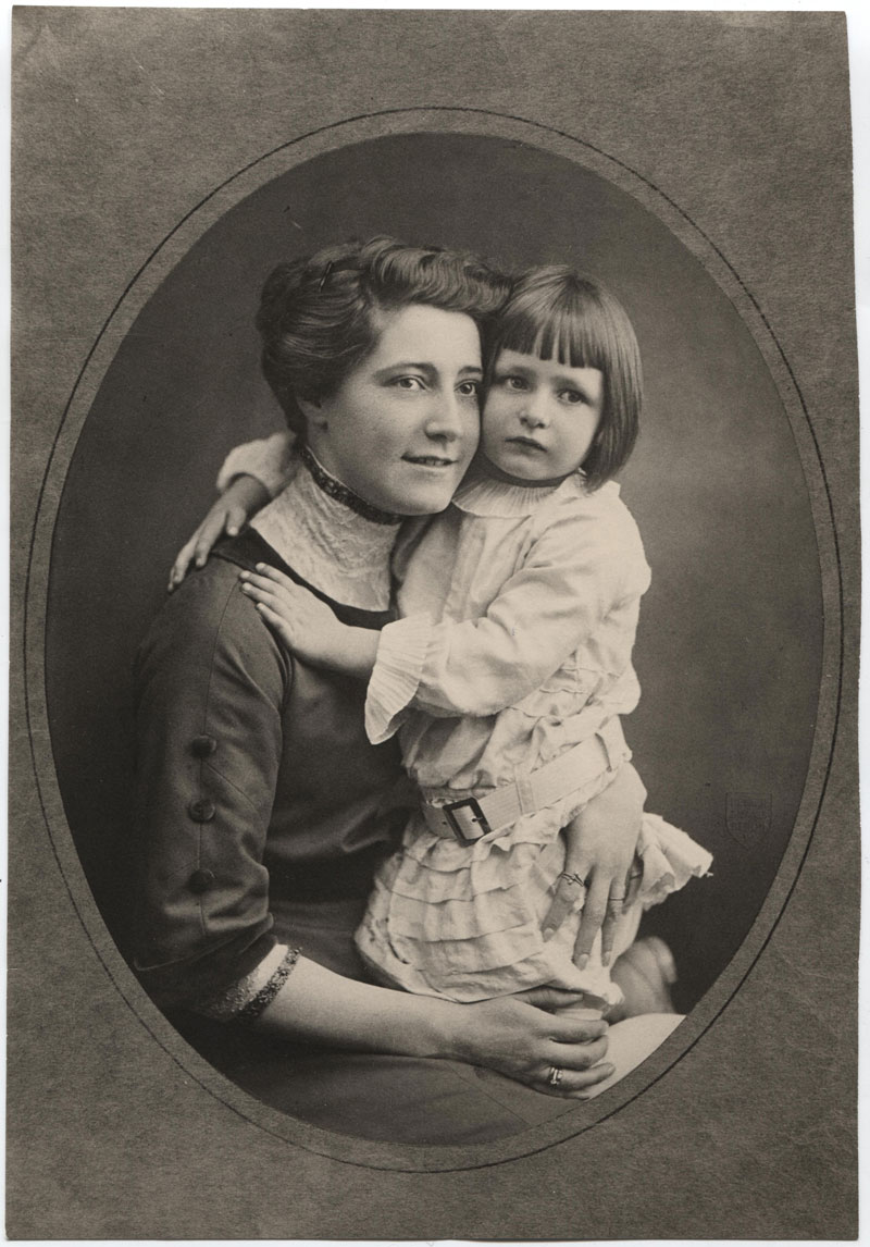 Porträtaufnahme von einer Mutter, die sitzt und ihrer kleinen Tochter, die auf ihrem Schoß sitzt und sie umarmt: Tilly und Pamela Wedekind.
