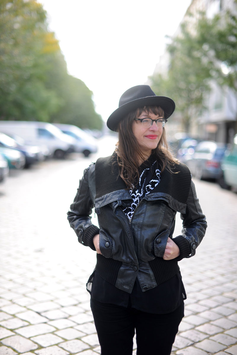Frau mit dunklen Haaren und schwarzen Hut auf einer Straße, trägt Brille und dunkle Kleidung: Ulli Lust, Comiczeichnerin.