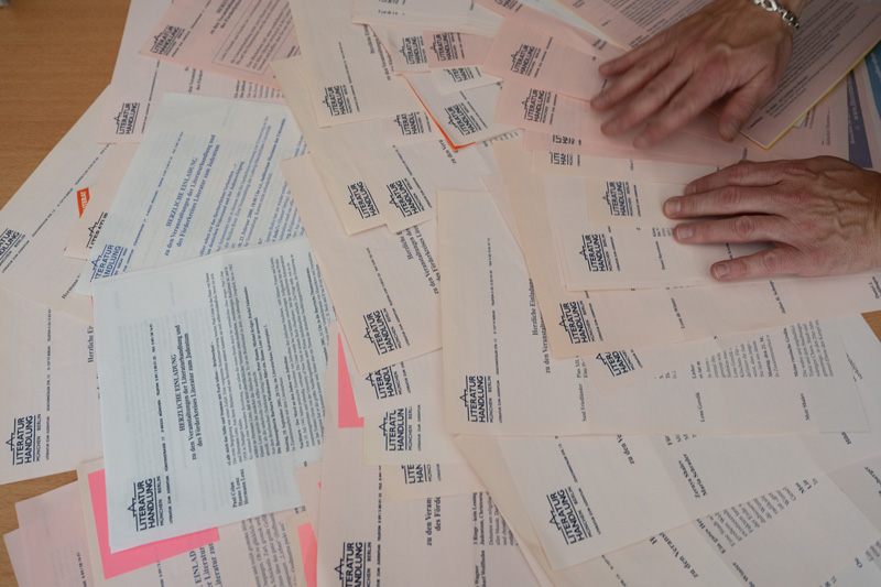 Auf Tisch ausgebreitete Veranstaltungsprogramme der Literaturhanldung mit zwei Hände.