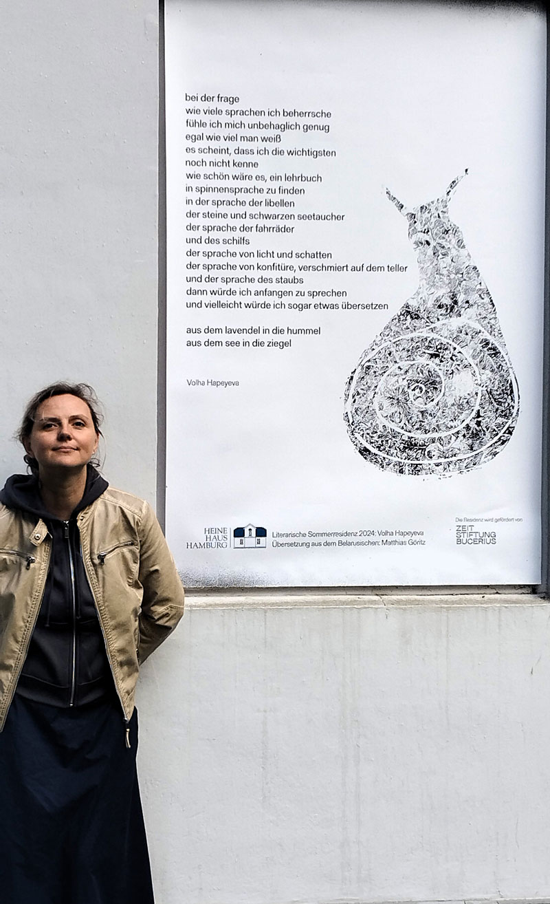 Volha Hapeyeva steht seitlich vor einem ihrer Gedichte mit Monotypie im Heine-Haus Hamburg